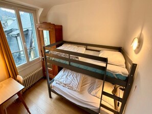 Ein Schlafraum mit Etagenbett, Fenster, Heizkörper und Schreibtisch.