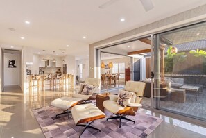 A modern interior with a dining area, kitchen, and a glass door leading to an outdoor space. - Burleigh Waters Luxury Getaway - Pool & Lake Views (Burleigh Waters)