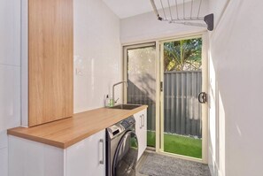 A compact kitchen with a built-in washing machine, a sink, and a drying rack. - Burleigh Waters Luxury Getaway - Pool & Lake Views (Burleigh Waters)