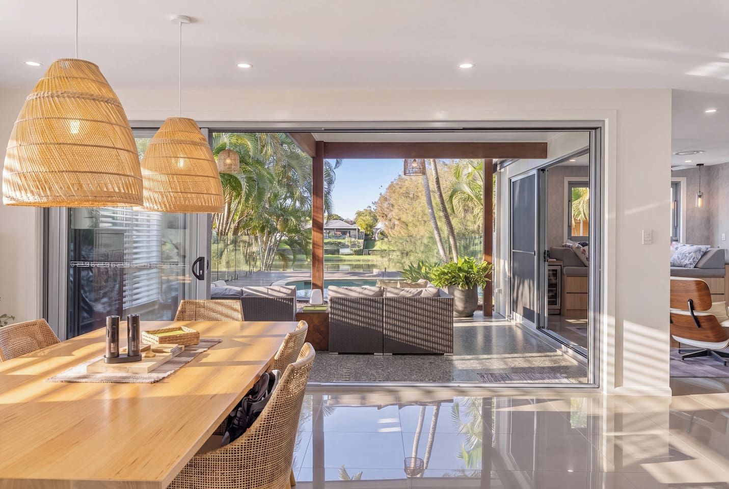 A modern interior with a dining area, wicker furniture, and a view of a pool and garden.