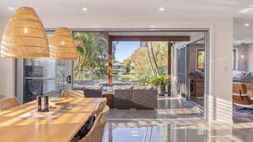 A modern interior with a dining area, wicker furniture, and a view of a pool and garden.