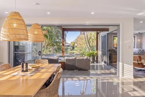 A modern interior with a dining area, wicker furniture, and a view of a pool and garden. - Burleigh Waters Luxury Getaway - Pool & Lake Views (Burleigh Waters)