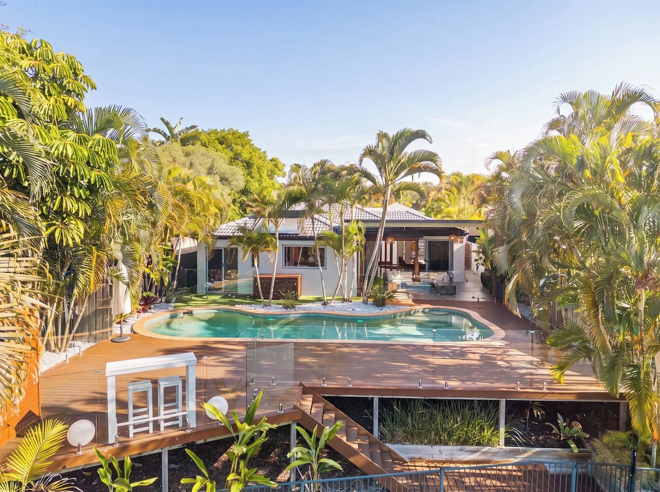 Un área de piscina con una casa al fondo, rodeada de vegetación tropical.