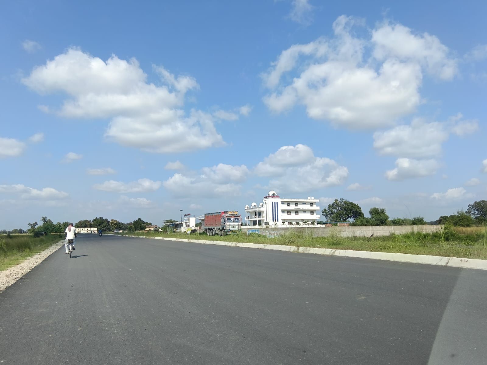 A wide road with buildings in the distance, a clear sky, and a person walking.