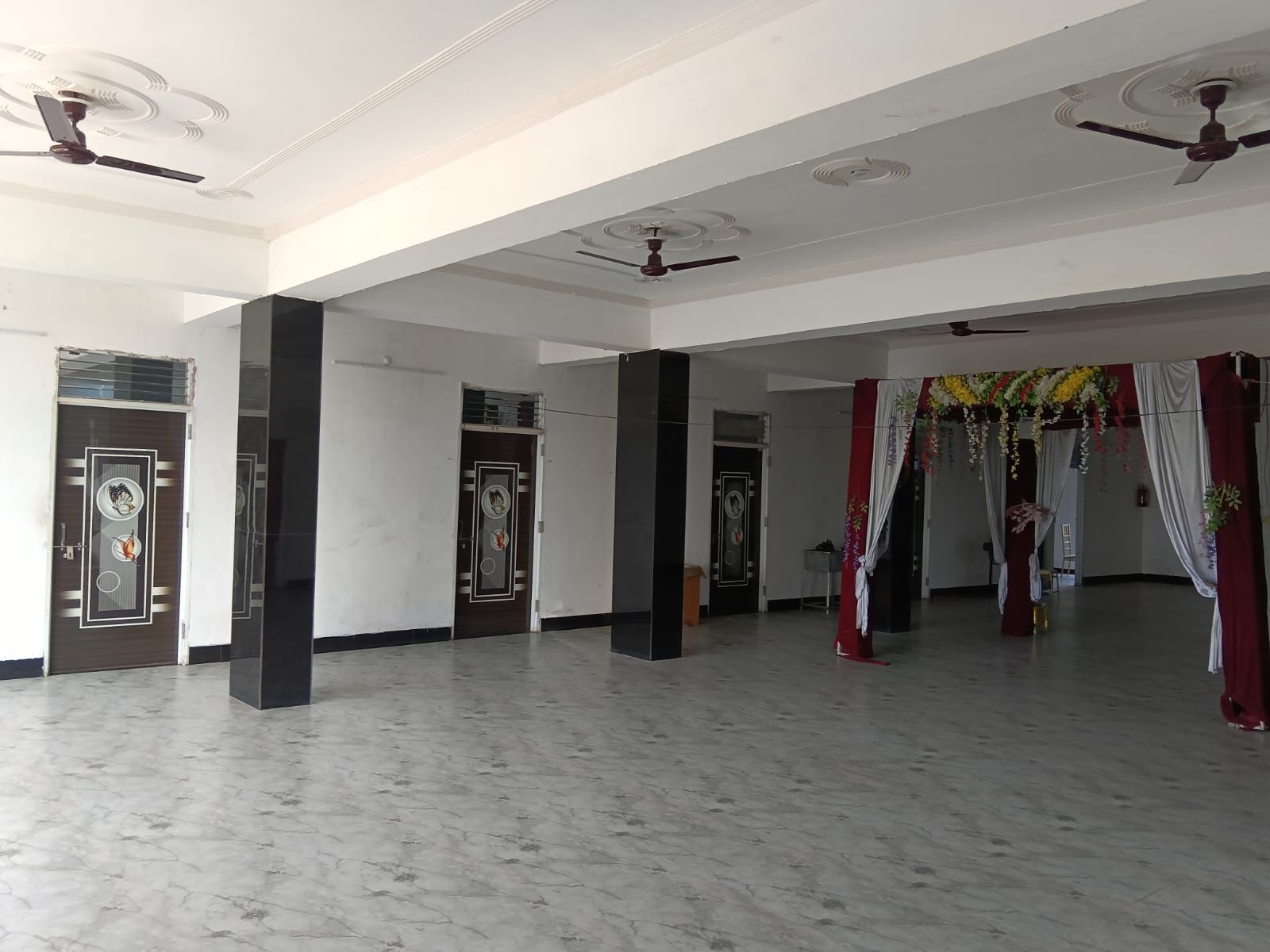 A spacious hall with marble flooring, ceiling fans, and decorative curtains.