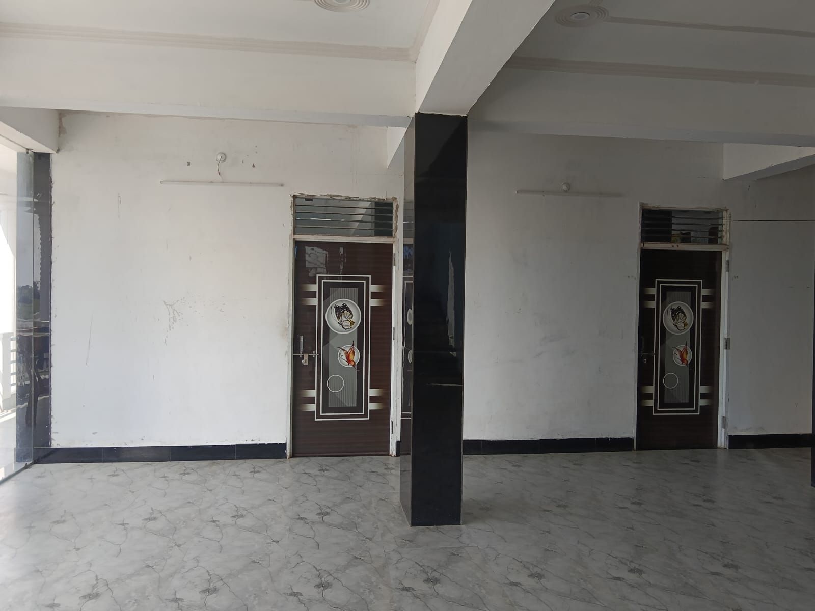 A spacious room with a marble floor, two doors with decorative glass panels, and a black pillar.