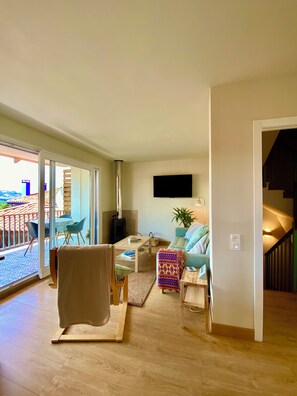 A living room with a sofa, a coffee table, and a TV. There is a sliding glass door leading to an outdoor area with a view. - Cosy Asturian home 10 minutes from Rodiles & Villaviciosa - pet friendly! (Villaviciosa)