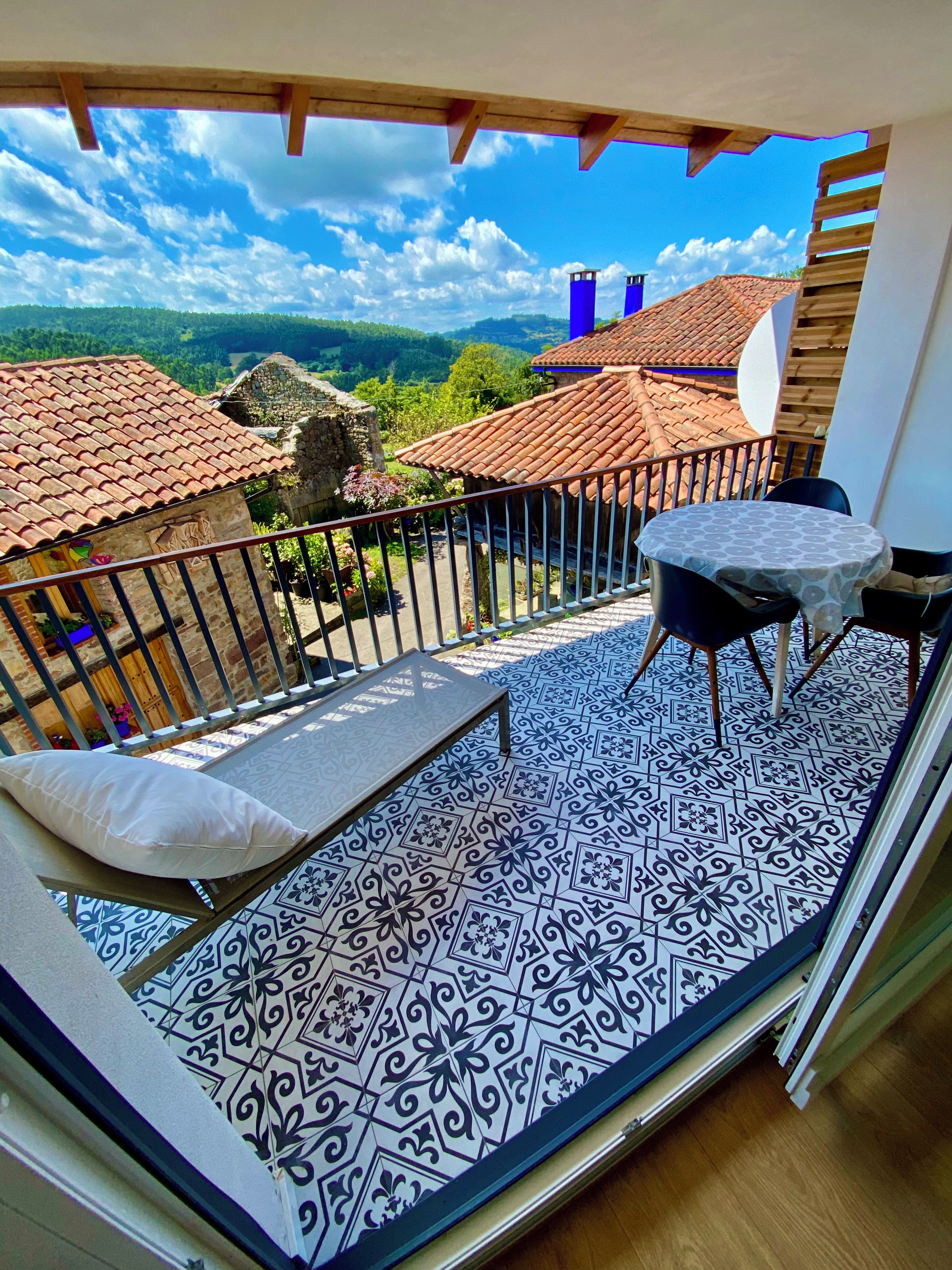 Un balcón con piso estampado, una mesa con sillas y vistas del paisaje circundante.