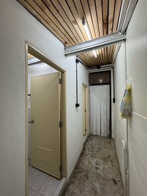 A narrow hallway with a wooden ceiling, a beige door, and a white wall with a utility box. - good night hostel (Krabi)