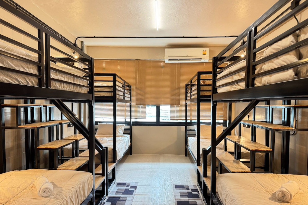 Une chambre avec des lits superposés, une fenêtre avec des stores, un appareil de climatisation et un tapis à motifs.