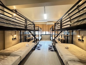 Un dortoir avec des lits superposés, un couloir central et une fenêtre avec des stores.