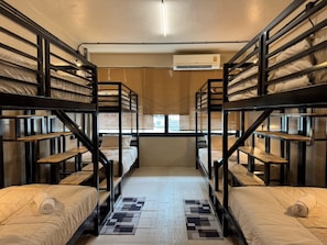 Une chambre de dortoir avec des lits superposés, une fenêtre avec des stores, un appareil de climatisation et un tapis à motifs.