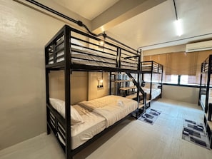 Une chambre avec un lit superposé, un plancher en bois, une lampe fixée au mur et une fenêtre avec des stores.
