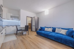 Ein modernes Wohnzimmer mit Küchenzeile, einem blauen Sofa und einem Essbereich.