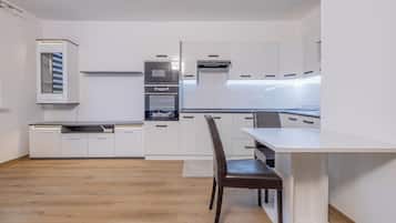 Una cocina moderna con armarios blancos, horno empotrado y comedor con mesa y sillas.