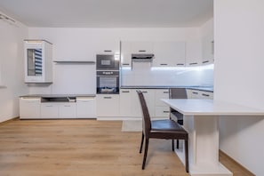 Eine moderne Küche mit weißen Schränken, einem Einbauofen und einem Essbereich mit Tisch und Stühlen.
