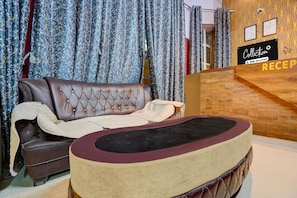 A reception area with a wooden reception desk, a brown leather sofa, and a patterned curtain backdrop. - Deluxe The Golden Sunrise (Danapur)