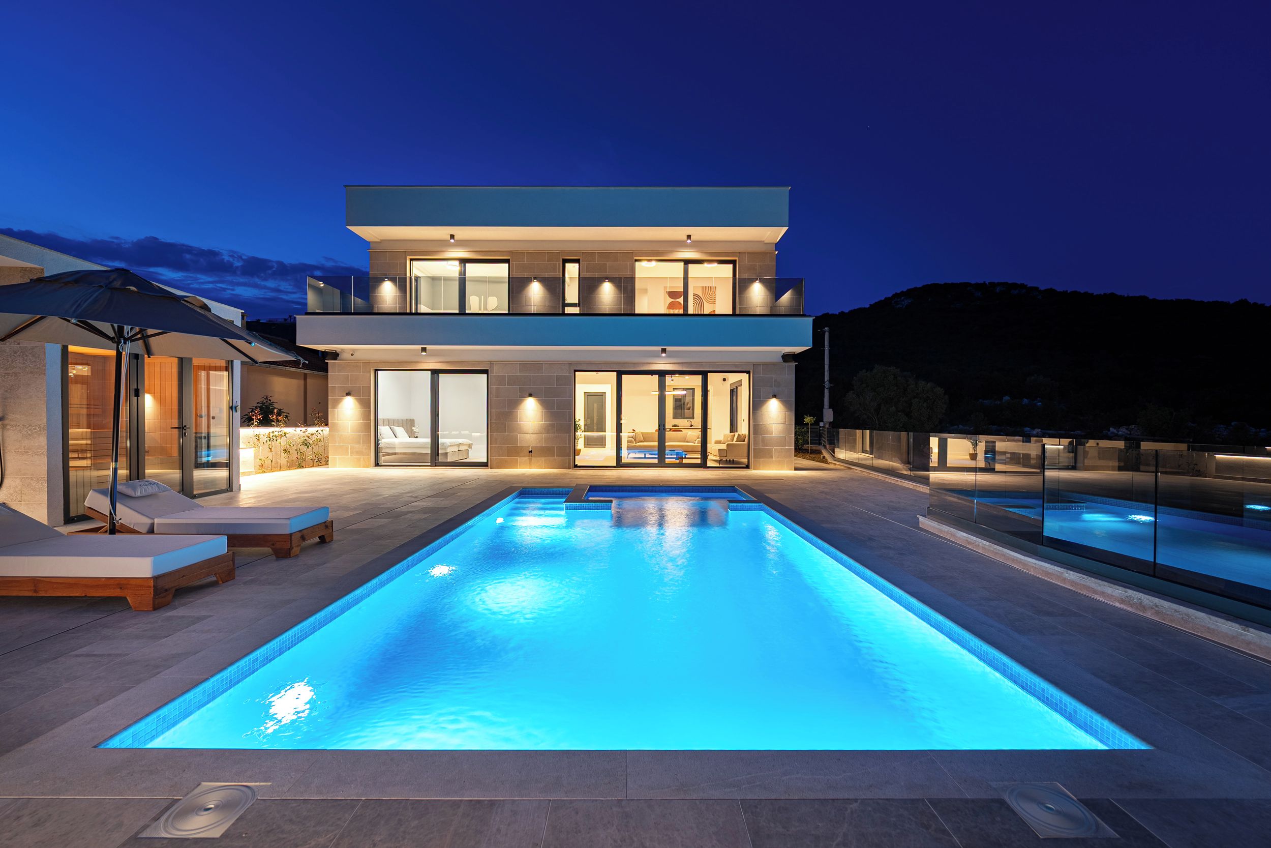Ein modernes, zweistöckiges Haus mit Swimmingpool, Sitzgelegenheiten im Freien und Blick auf die umliegende Landschaft.