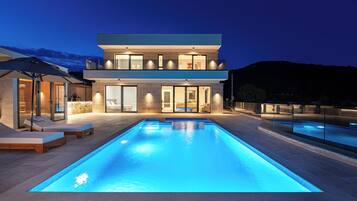 Ein modernes, zweistöckiges Haus mit Swimmingpool, Sitzgelegenheiten im Freien und Blick auf die umliegende Landschaft.