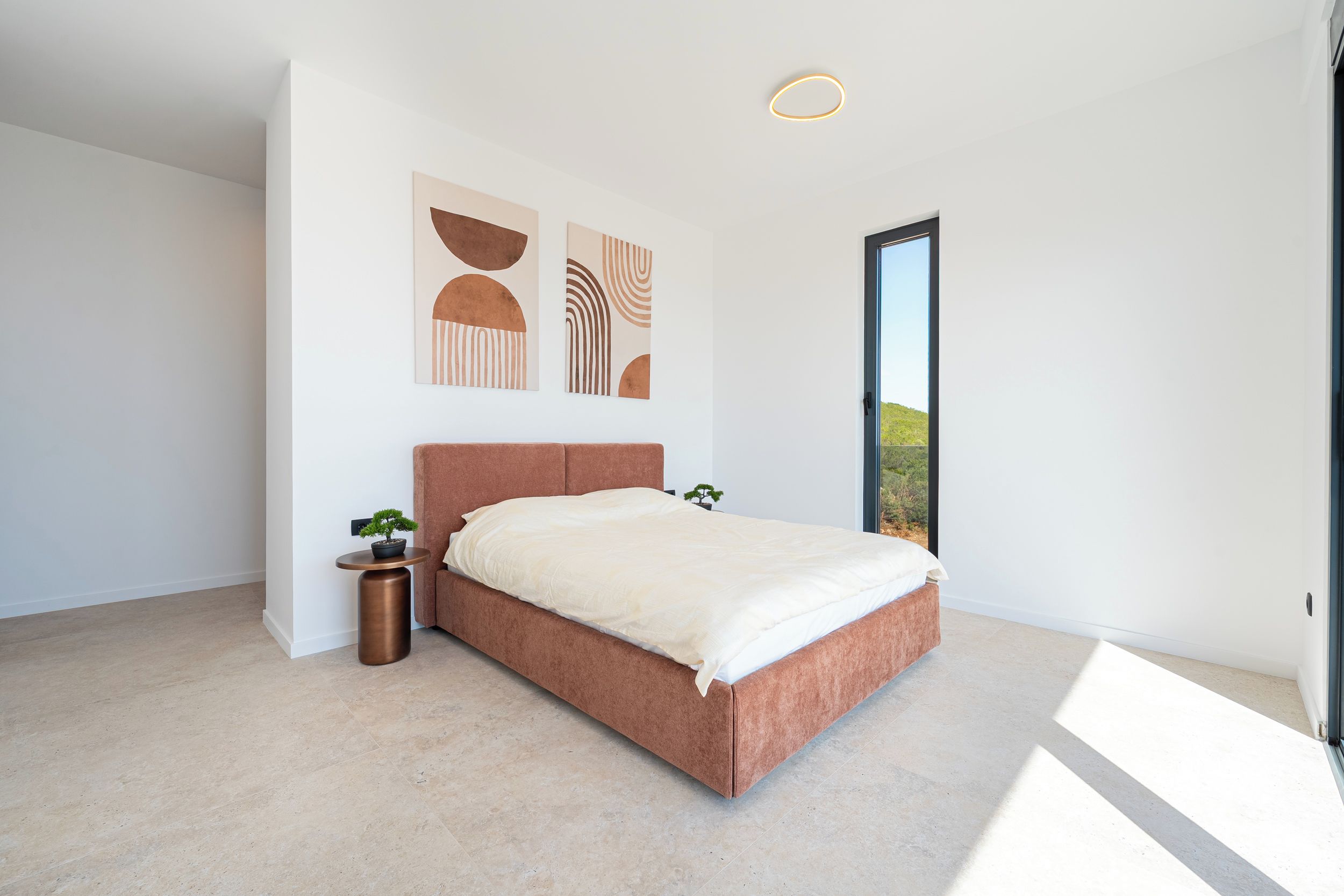 Un dormitorio moderno con una cama grande, una mesita de noche con una planta y arte abstracto en la pared.