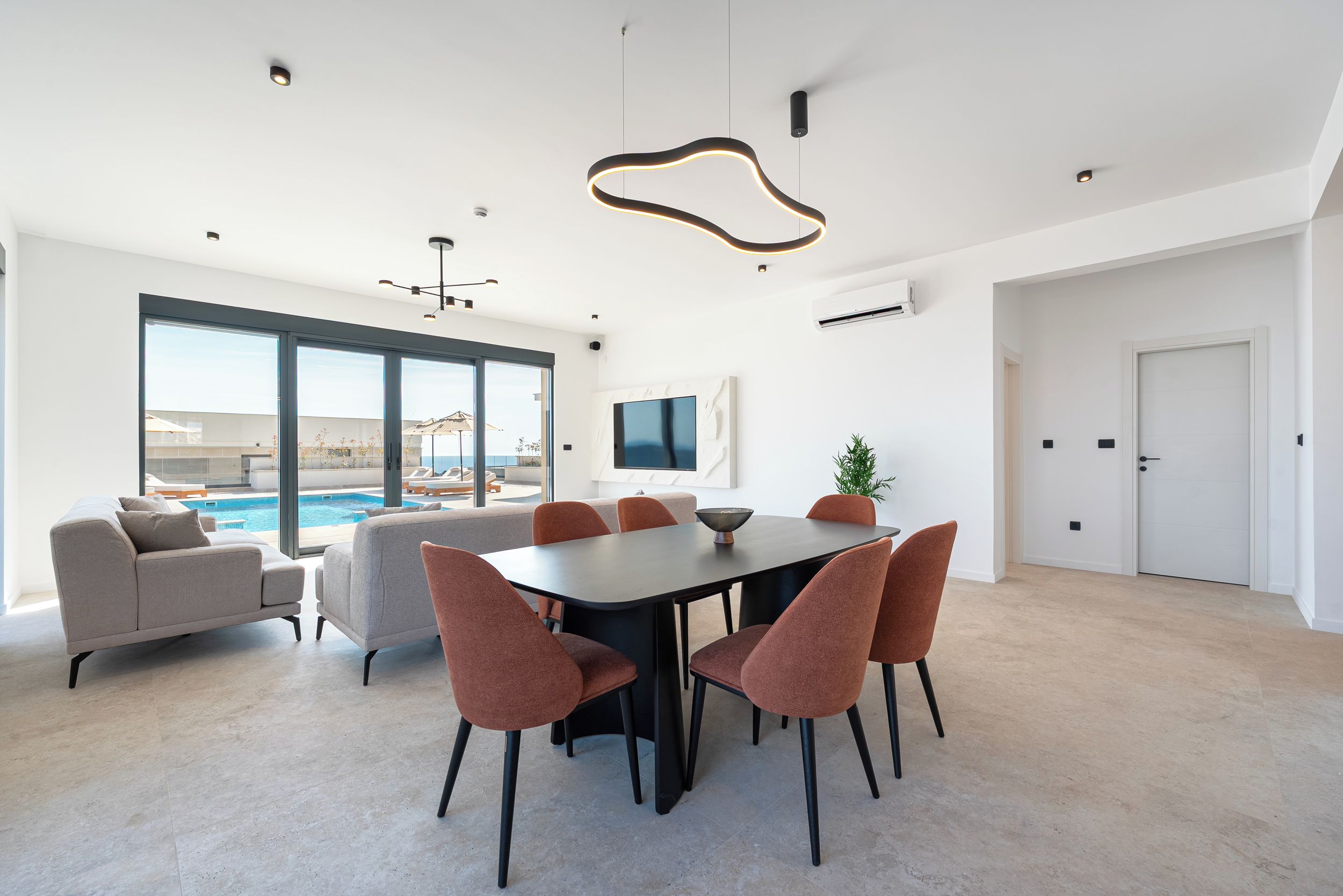 A modern dining area with a pool view, a flat-screen TV, and a minimalist design.