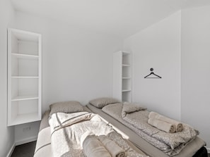 A minimalist bedroom with two beds, a wardrobe, and a towel rack. - "Apsolon" - 50m to the fjord by Interhome (Tarm)