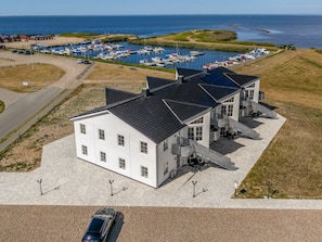 Een wit gebouw met een plat dak, een overdekt terras en een jachthaven op de achtergrond.