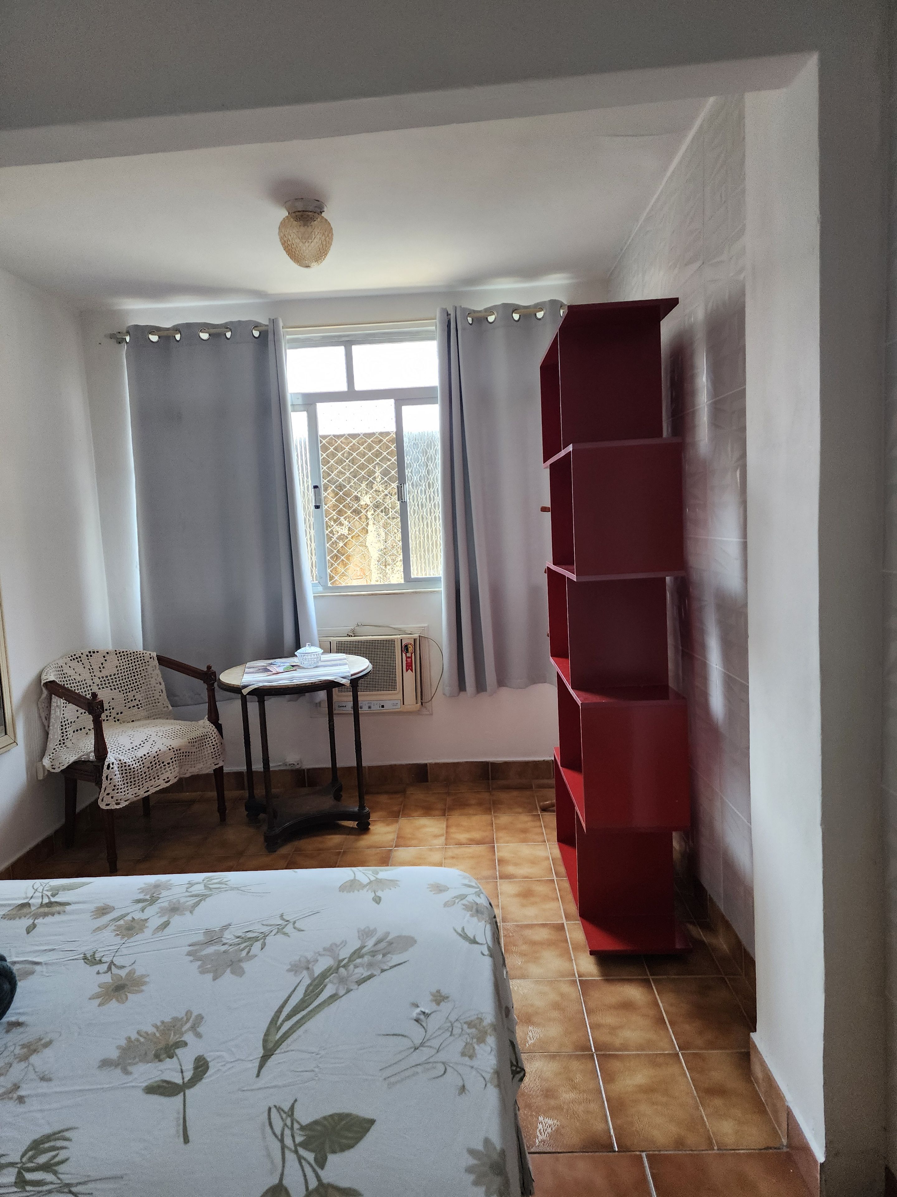 A room with a bed, a table with a chair, a radiator, and a red shelving unit.