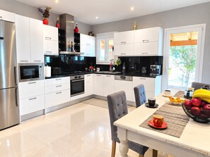 A modern kitchen with white cabinetry, stainless steel appliances, and a dining area with a table set for breakfast. - La Casa Di Kosta dream house in Kontogialos (Kontogialos)
