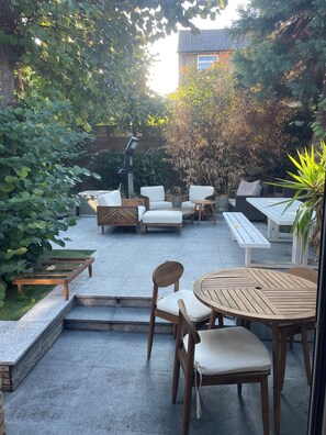 An outdoor patio with seating arrangements, a pergola, and a view of a building in the background. - Modern four story house In Canonbury / Islington (London)