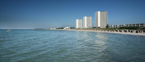 Una propiedad frente al mar con una terraza de madera, una hilera de edificios frente a la playa y una vista despejada del océano.