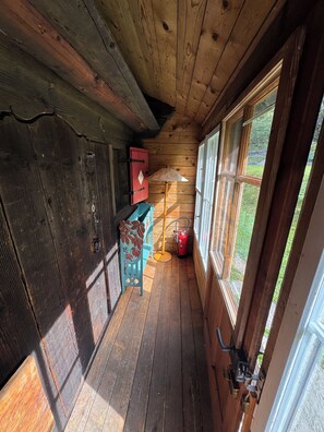 A wooden cabin interior with a wooden floor, a red cabinet, a blue chair, a table lamp, and a window with a view of greenery. - Authentic chalet for mountain lovers - near to Portes du Soleil skiing area (Val-d'Illiez)