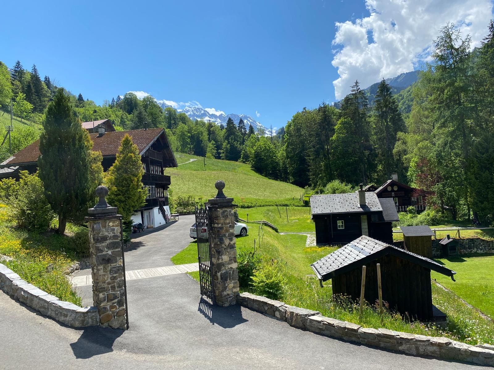 A mountain lodge with a stone entrance gate, wooden buildings, and a view of snow-capped mountains.