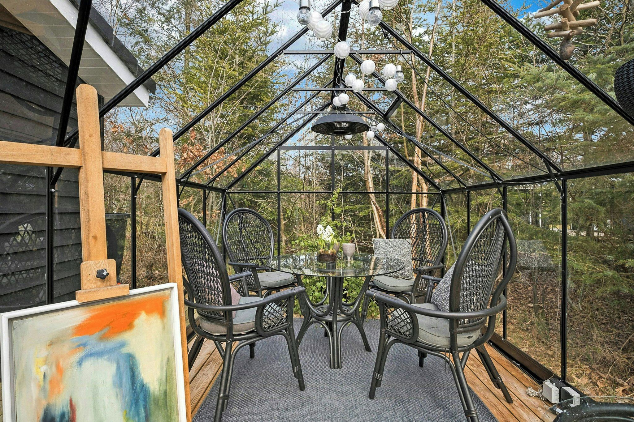 Een glazen terras omgeven door bomen, met een tafel en stoelen.