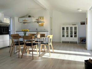 A modern kitchen with a dining area, wooden flooring, and a cabinet with glass doors. - Timber deck with hot tub near Alsodde (Hadsund)