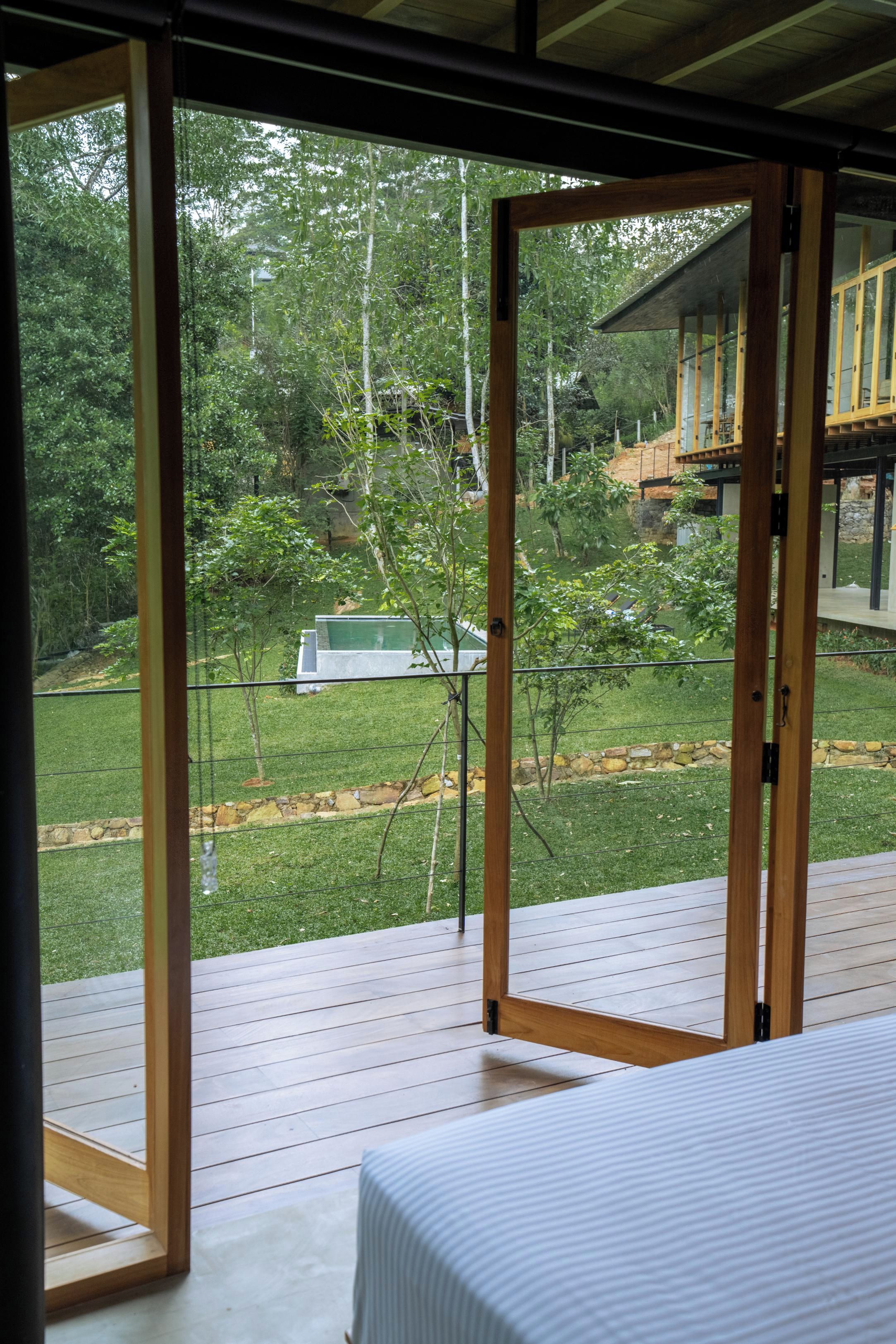 A room with a bed, a wooden deck, and a view of a garden and trees.