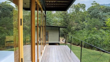 A wooden deck with a glass enclosure, overlooking a lush green landscape.