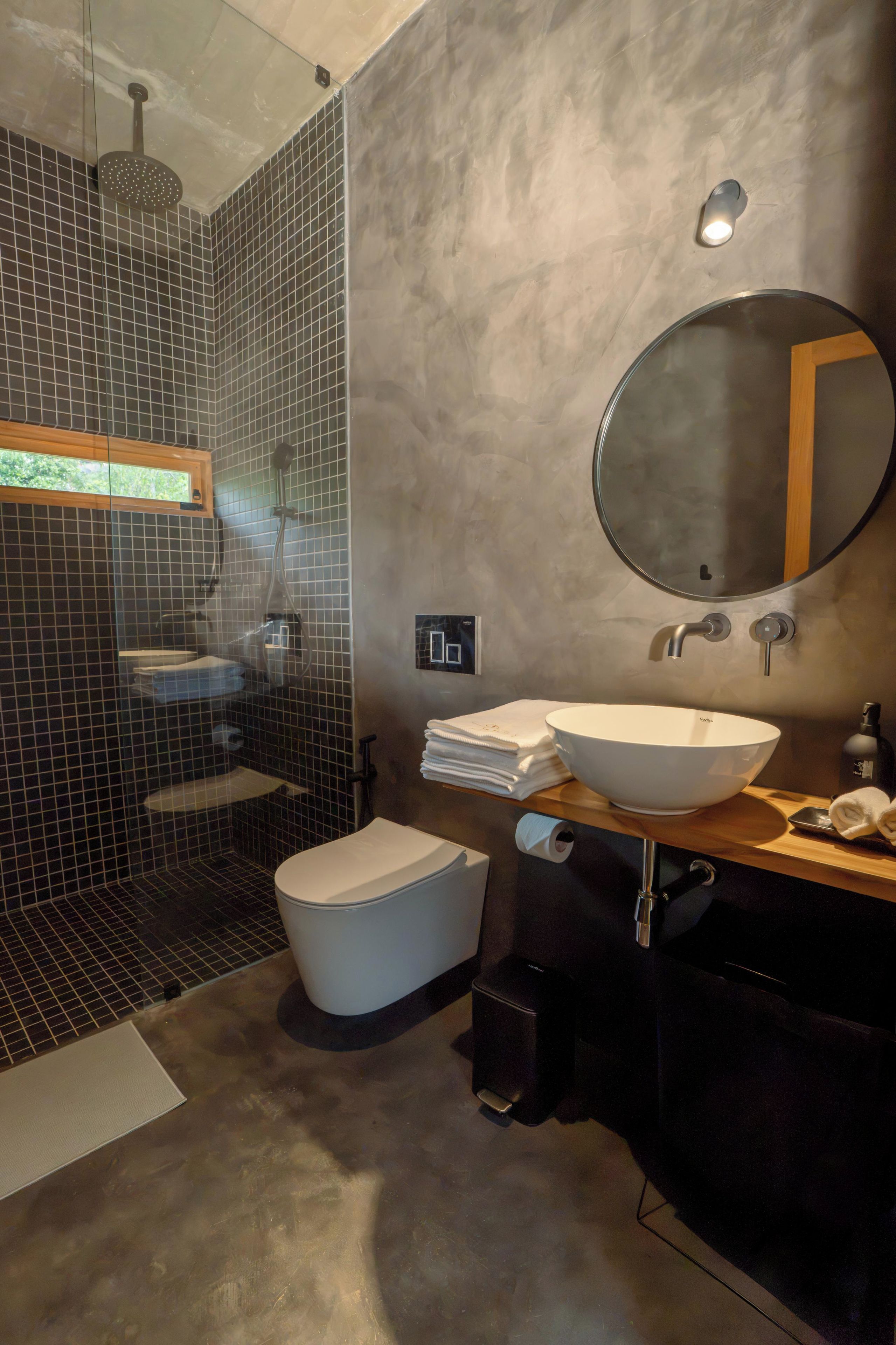 Un baño moderno con ducha de vidrio, inodoro blanco, lavamanos y espejo.