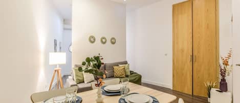 A dining area with a table set for four, a sofa, and a wooden wardrobe.
