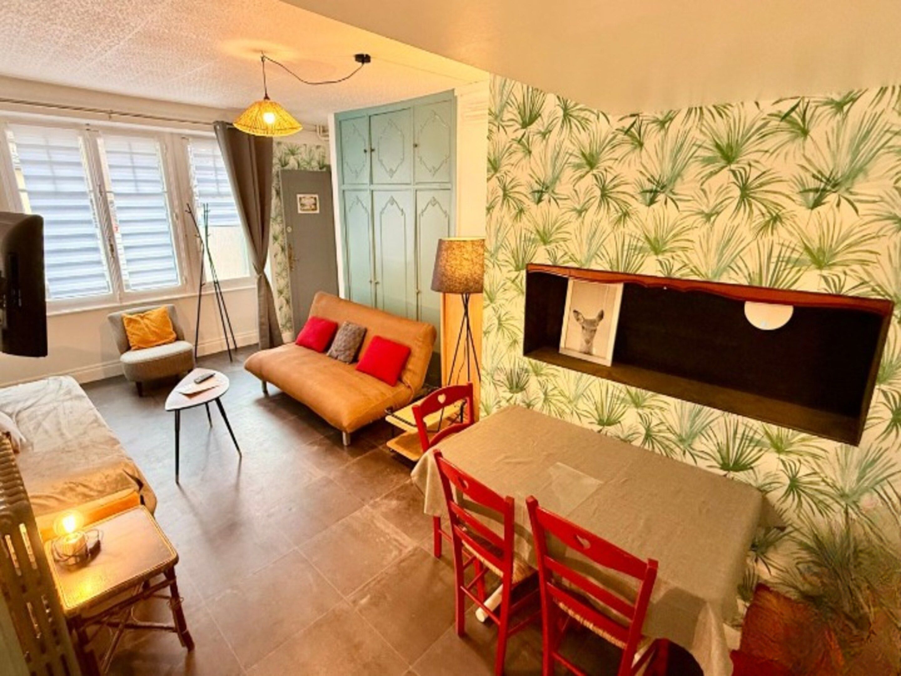 A cozy living room with a sofa, a dining table with chairs, a TV, and a patterned wall.