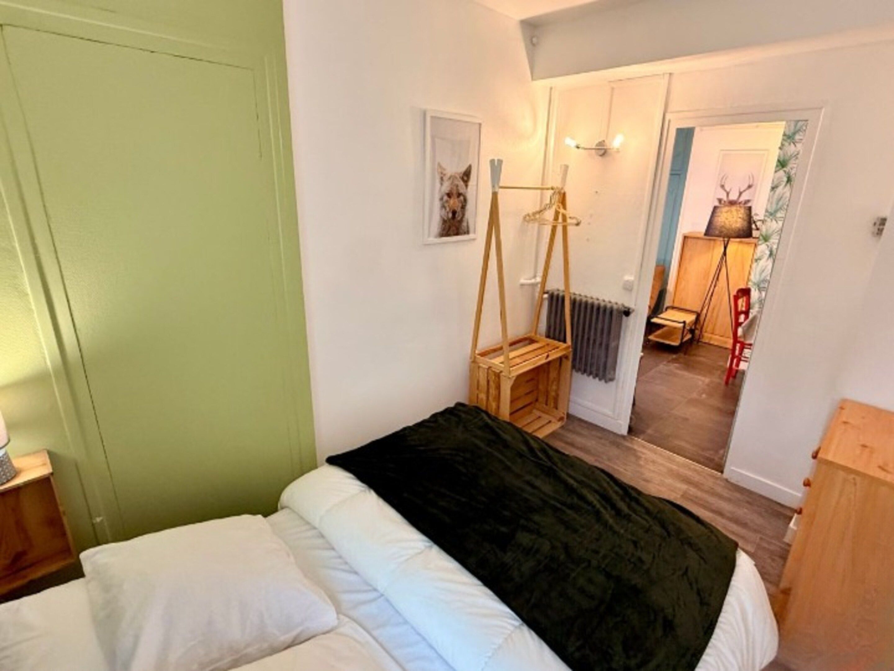 A bedroom with a bed, a wooden side table, a radiator, and a door leading to another room.