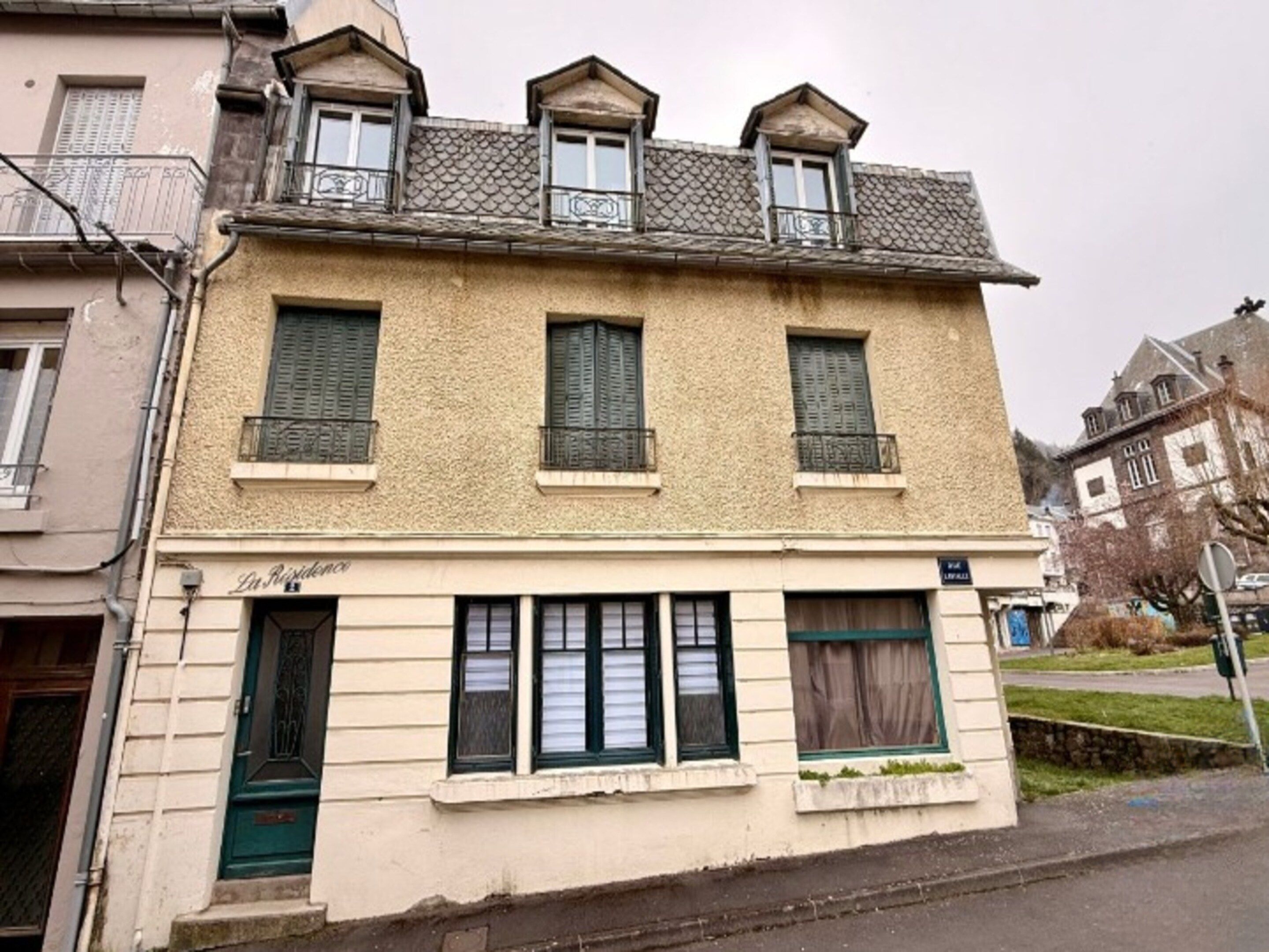 A two-story building with a flat facade, multiple windows with shutters, and a visible entrance.