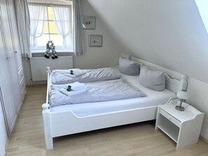 A white, single-bed room with a wooden floor, a bedside table with a lamp, and a window with curtains. - Holiday Home in Wrixum With Terrace (Wrixum)