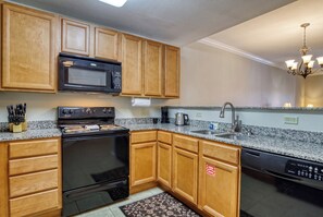 A kitchen with wooden cabinets, a black stove, a microwave, a sink, and a dishwasher. - Cozy Pigeon Forge Condo | Mountain Views, Resort Pools & Near Dollywood (Pigeon Forge)