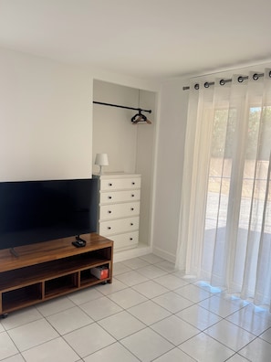 A room with a flat-screen TV on a wooden stand, a white dresser with drawers, a coat rack, and a window with sheer curtains. - Apartment 50 meters from the beach, ideal for 4 people (Palavas-les-Flots)