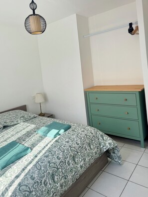 A bedroom with a bed, a nightstand, a lamp, a dresser, and a hanging light fixture. - Apartment 50 meters from the beach, ideal for 4 people (Palavas-les-Flots)