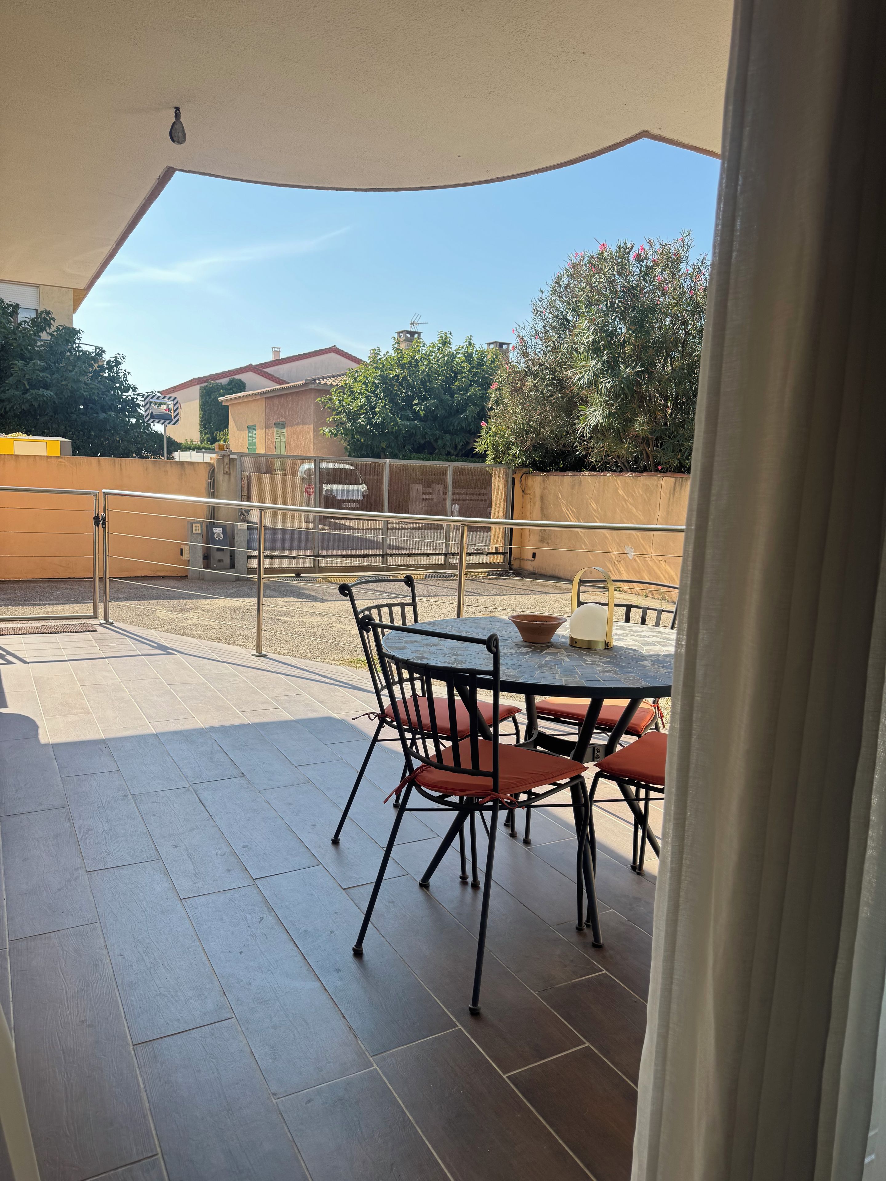 A patio area with a round table and chairs, a covered seating area, and a view of the surrounding neighborhood.