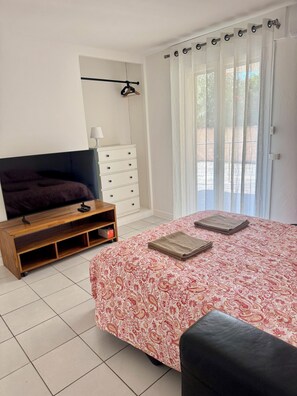 A bedroom with a bed, a wooden TV stand, a white dresser, and a window with sheer curtains. - Apartment 50 meters from the beach, ideal for 4 people (Palavas-les-Flots)