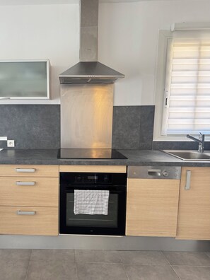 Eine moderne Küche mit integriertem Backofen, Geschirrspüler und einem Fenster mit Jalousien.