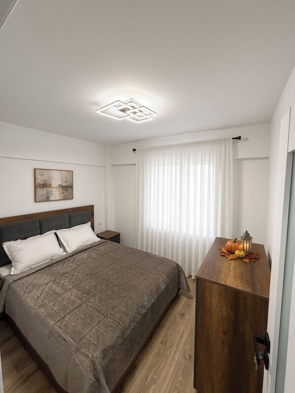 A bedroom with a bed, a nightstand, a wooden dresser, a painting on the wall, and a window with curtains. - APARTAMENT CENTRAL HARSOVA - 3 BEDROOMS (Hârșova)